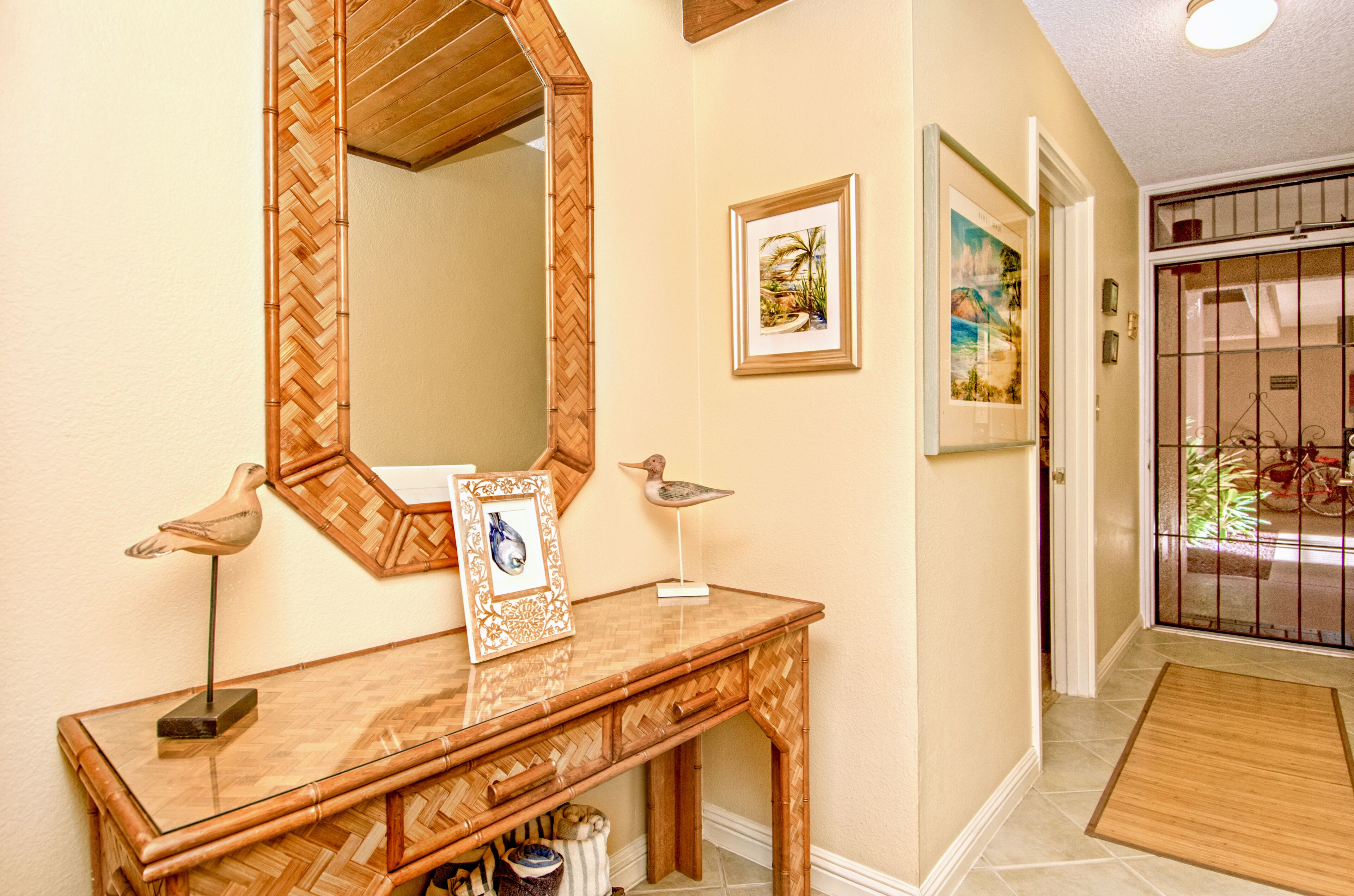 A wooden console table with a mirror, framed pictures, and a bird sculpture.