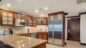 A kitchen with granite countertops, wooden cabinets with glass doors, stainless steel appliances, and a tiled backsplash.
