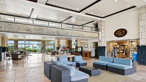 A spacious lobby with a high ceiling, a central seating area with sofas, a reception desk, and a visible store.