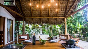 A covered outdoor dining area with a thatched roof, a sink, and a stove.