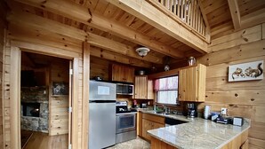A modern kitchen with wooden walls, a stone fireplace, stainless steel appliances, and a granite countertop. - Seclusion, perfect location, escape the crowds, pet friendly (Sevierville)
