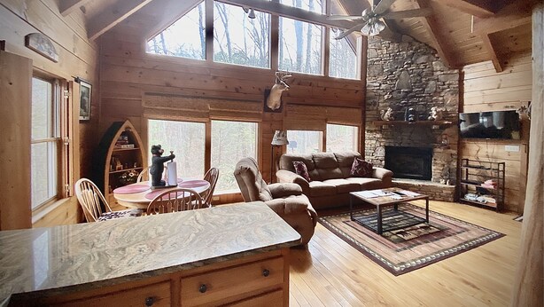 A cozy cabin interior with a stone fireplace, wooden furniture, and large windows. - Seclusion, perfect location, escape the crowds, pet friendly (Sevierville)