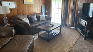 A cozy living room with a brown leather sofa, a wooden coffee table, and a television on a wooden cabinet. - Cozy beach cottage in Magnolia (Port Lavaca)