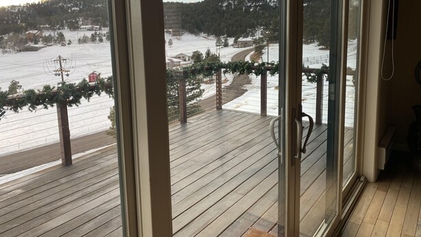 Une vue depuis un balcon avec une terrasse en bois, donnant sur un paysage enneigé avec des maisons et une montagne.