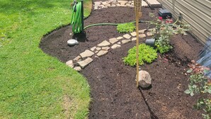 Ein angelegter Garten mit einem Kiesweg, einem Gartenschlauch und einer Laterne in der Nähe eines Hauses.