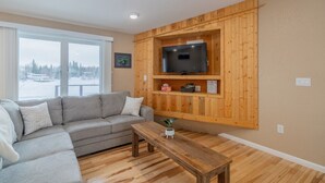 Ein Wohnzimmer mit einem grauen Ecksofa, einem Holztisch und einem an einer Holzwand befestigten Fernseher.