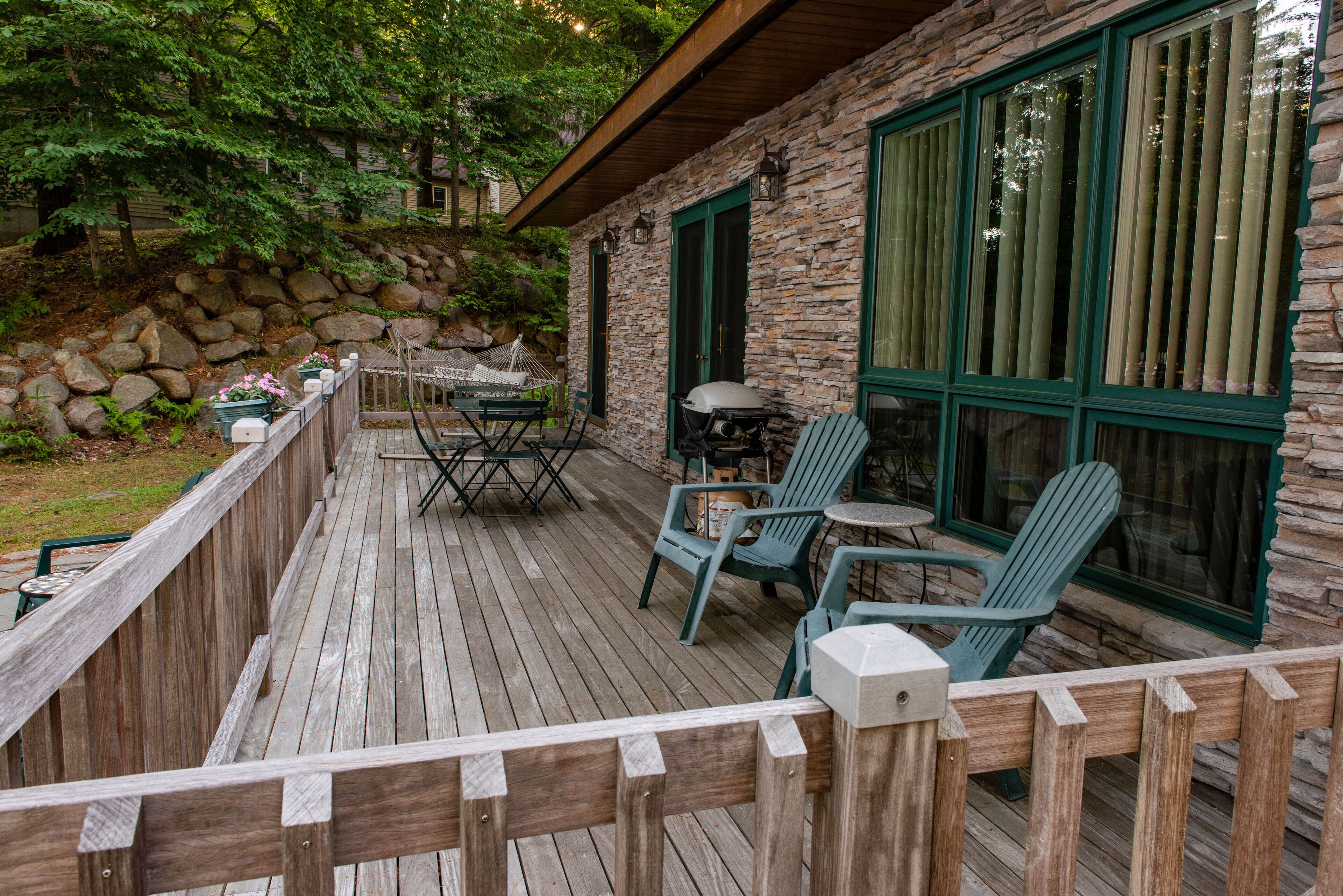 Une terrasse en bois avec des meubles d’extérieur, des murs en pierre et de grandes fenêtres.