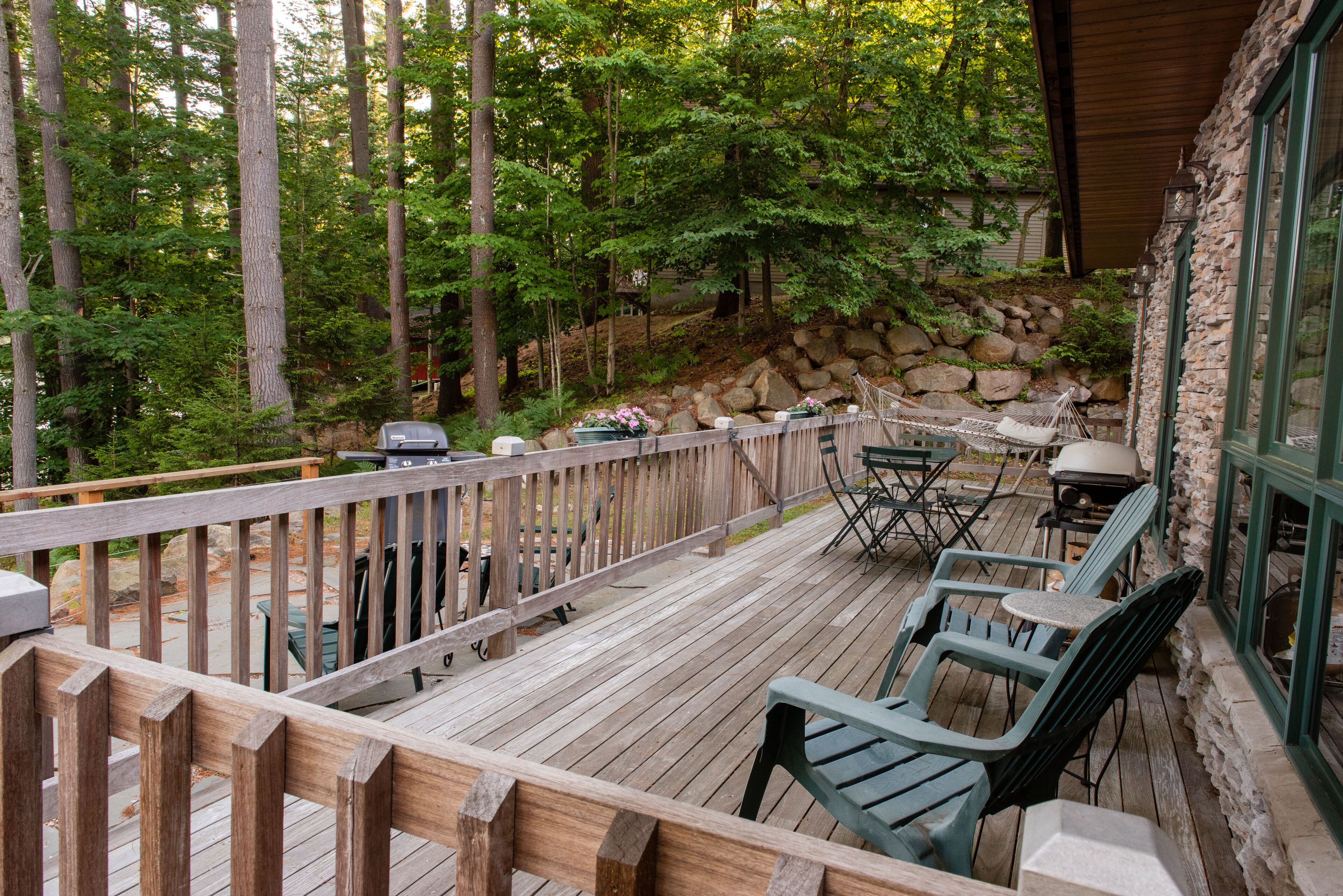 Une terrasse en bois avec des meubles d’extérieur, un mur en pierre et une vue sur une zone boisée.
