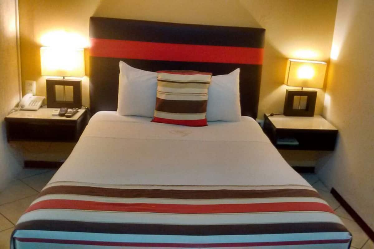 A hotel room with a bed, two bedside tables, a lamp, and a telephone on one of the tables.