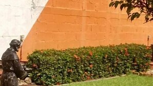 A statue of a man in a suit standing on a grassy area with a hedge and a brick wall in the background. - Madero Suites (Coatzacoalcos)