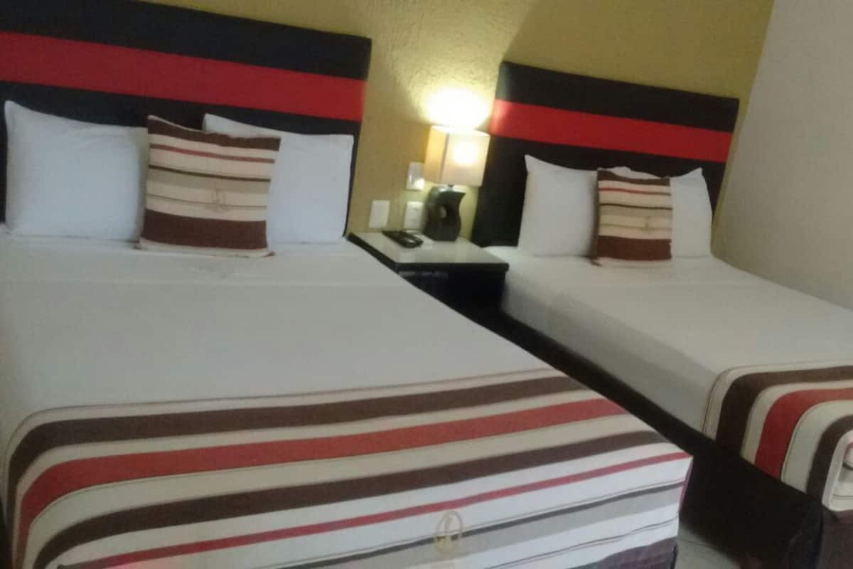 A hotel room with two single beds, each with striped bedding and pillows. There is a nightstand with a lamp and a telephone between the beds.