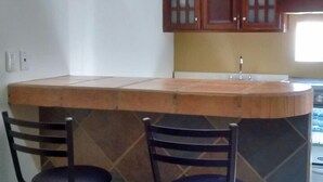 A kitchen with a wooden island, two bar stools, and a window. - Madero Suites (Coatzacoalcos)