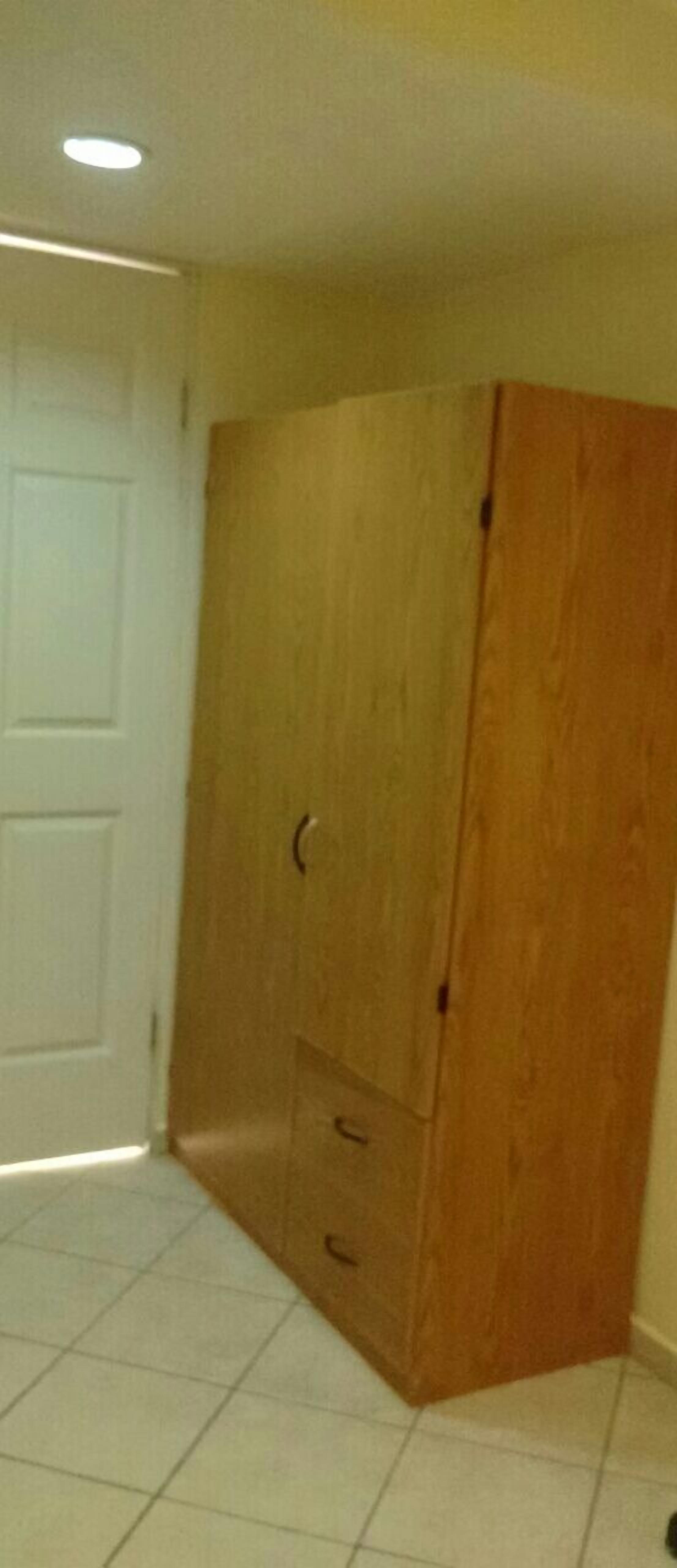 Una habitación con un armario de madera, piso de baldosas y una puerta blanca.