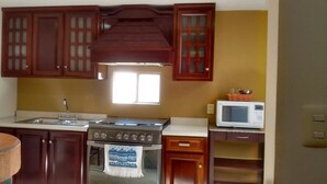 A kitchen with wooden cabinets, a stove, a microwave, and a window. - Madero Suites (Coatzacoalcos)