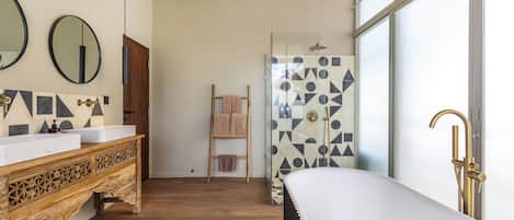 Un baño con tocador de madera, una bañera independiente y una ducha con diseños geométricos de azulejos.