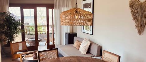 A spacious dining area with a round wooden table and chairs, a woven pendant light, and a sofa with cushions.