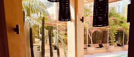 A cozy lounge area with a sofa, small tables, and a view of a pool and garden.