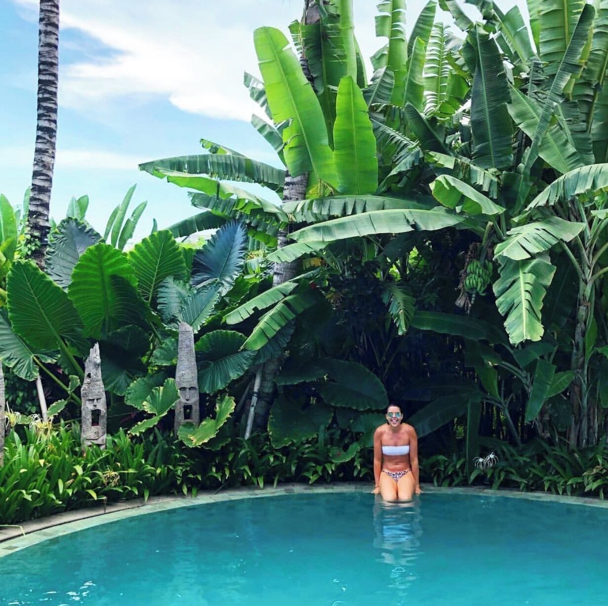 A woman in a bikini standing in a pool surrounded by lush tropical foliage.