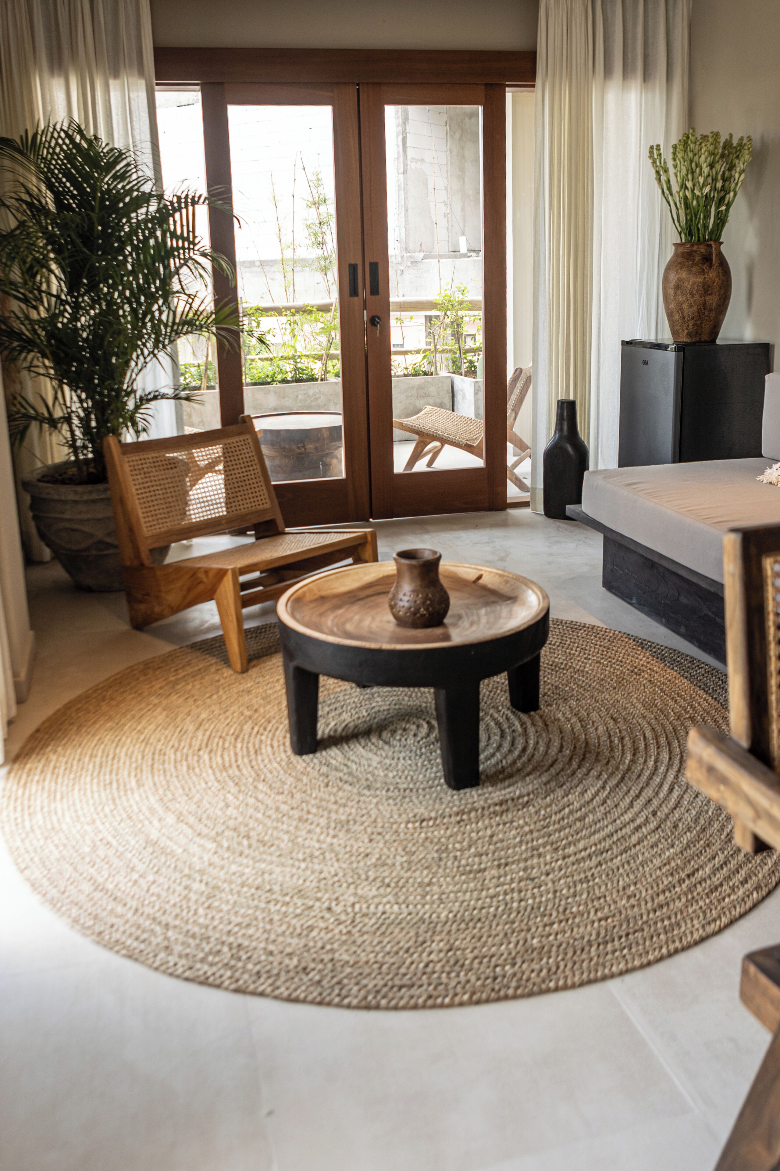 Une pièce comprenant un banc en bois, une table ronde avec un vase, une plante en pot et un canapé.