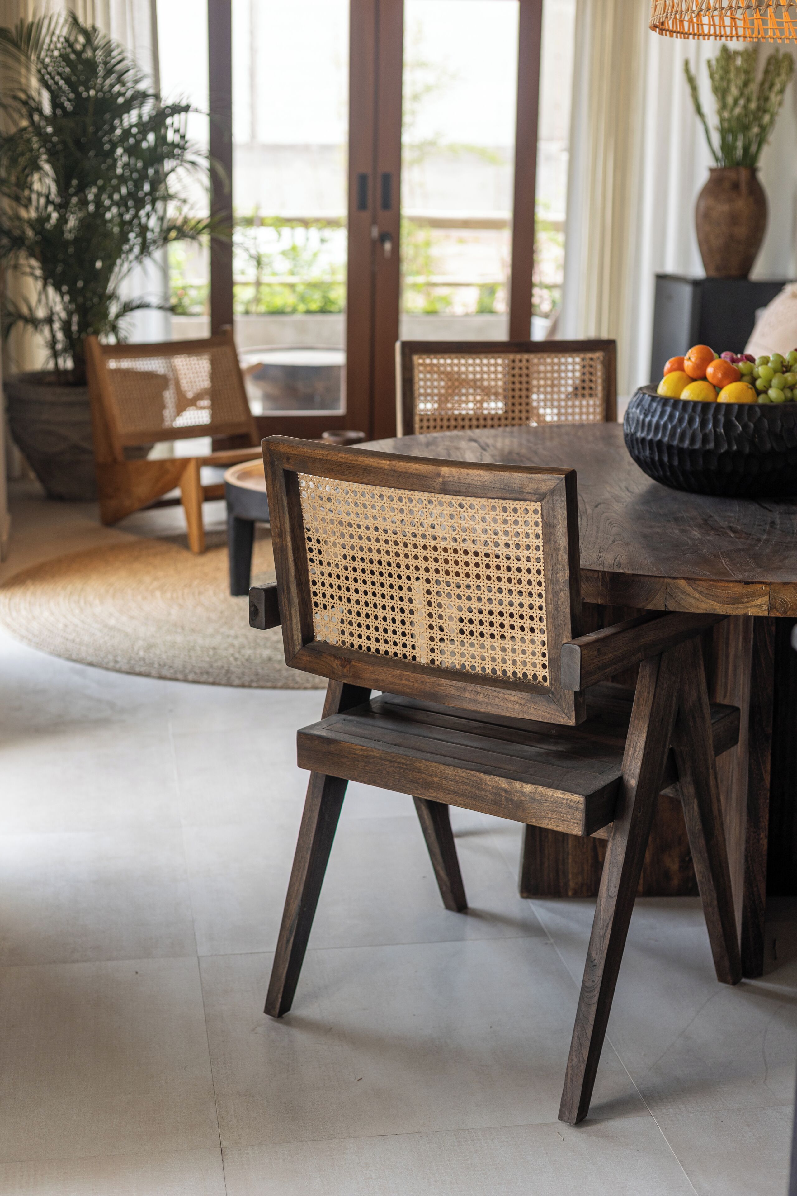 A dining area with a wooden table and chairs, a bowl of fruit, and a potted plant.