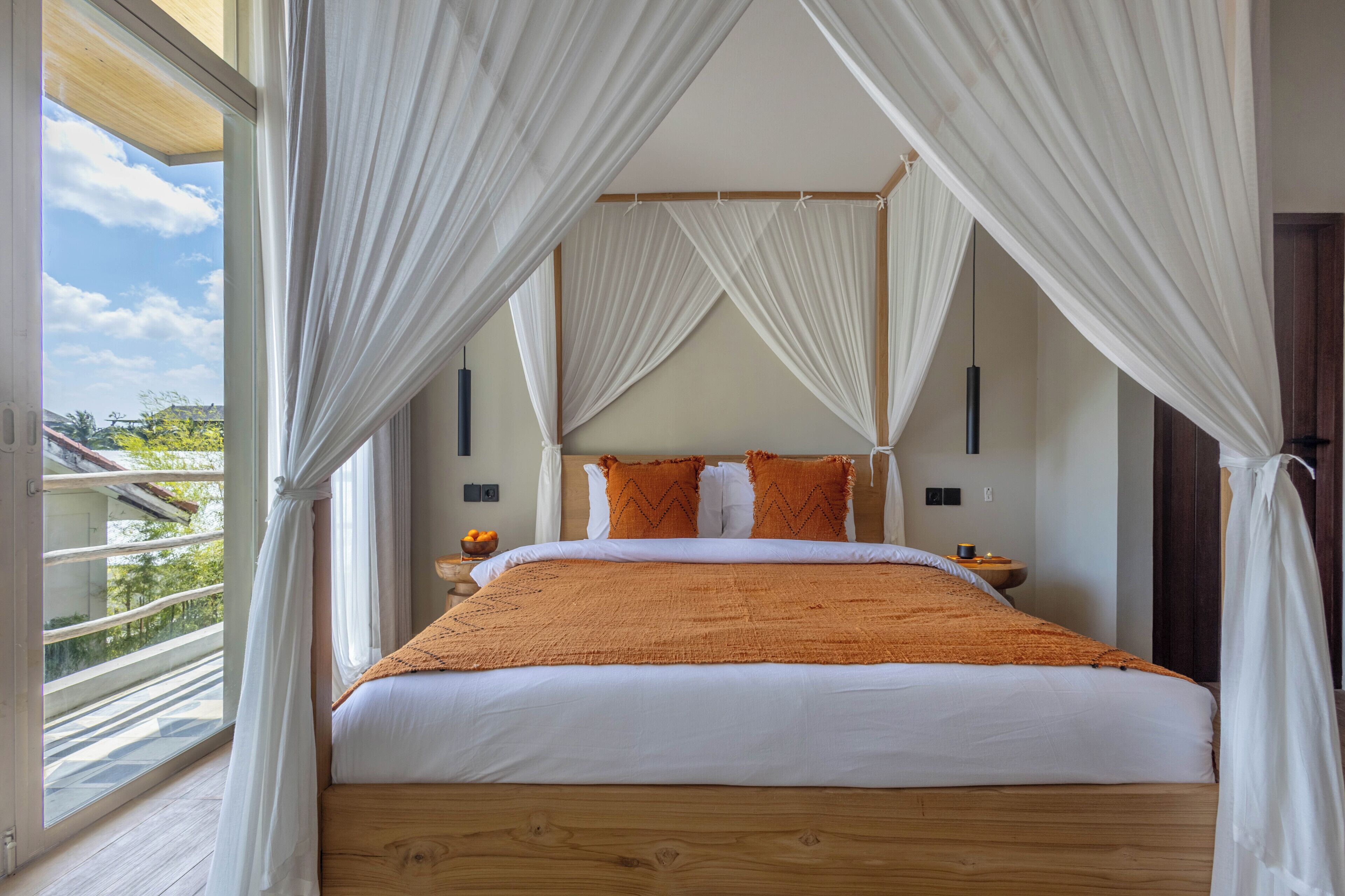 A bedroom with a large bed, white curtains, and a view of the outdoors.