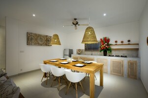 Uma cozinha moderna com uma mesa de jantar de madeira, cadeiras brancas, luminárias pendentes e um ventilador de teto.