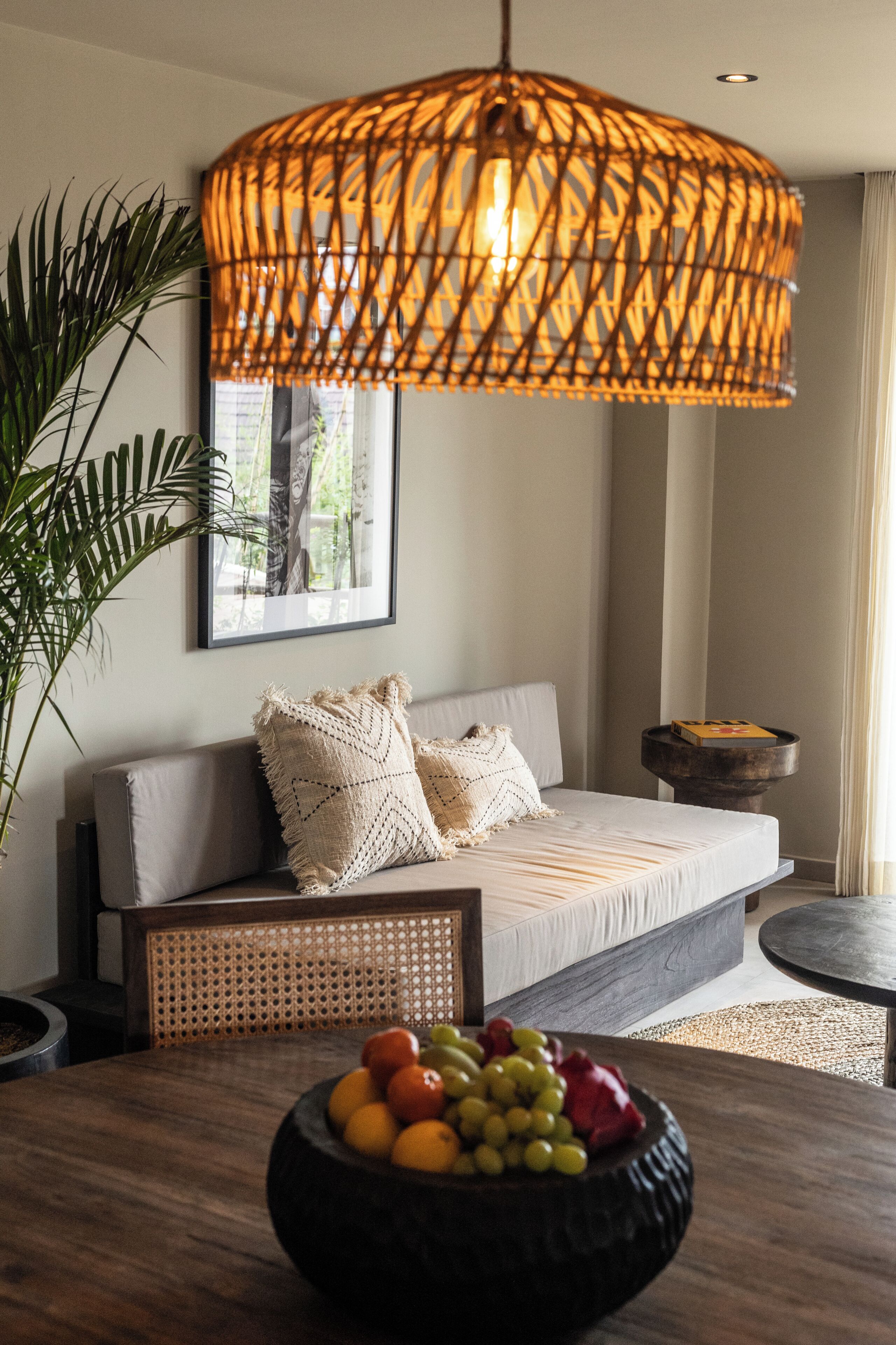 A modern living room with a sofa, a woven pendant light, a fruit bowl, and a framed picture on the wall.