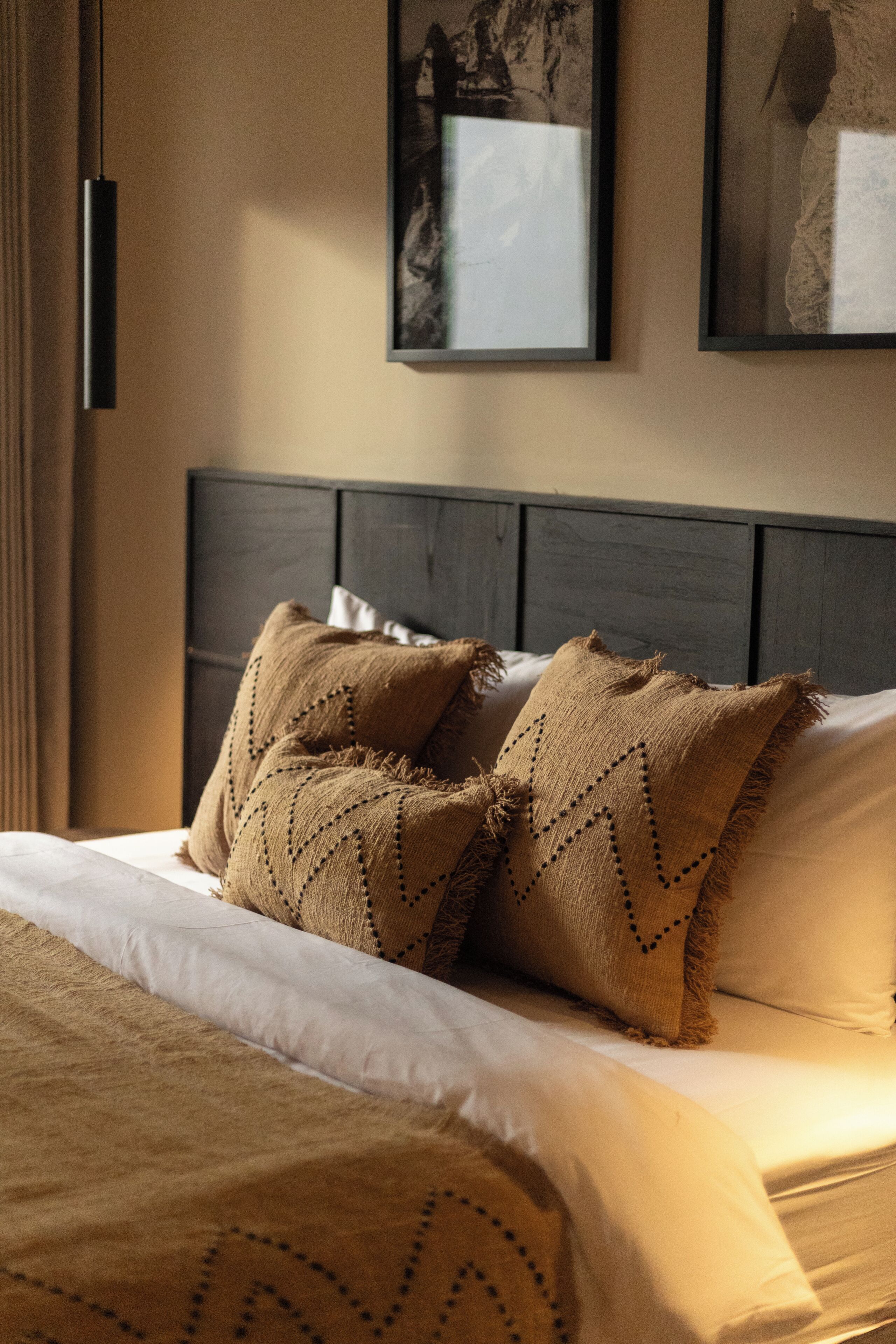 Uma cama com cabeceira escura, duas almofadas decorativas e um cobertor claro.