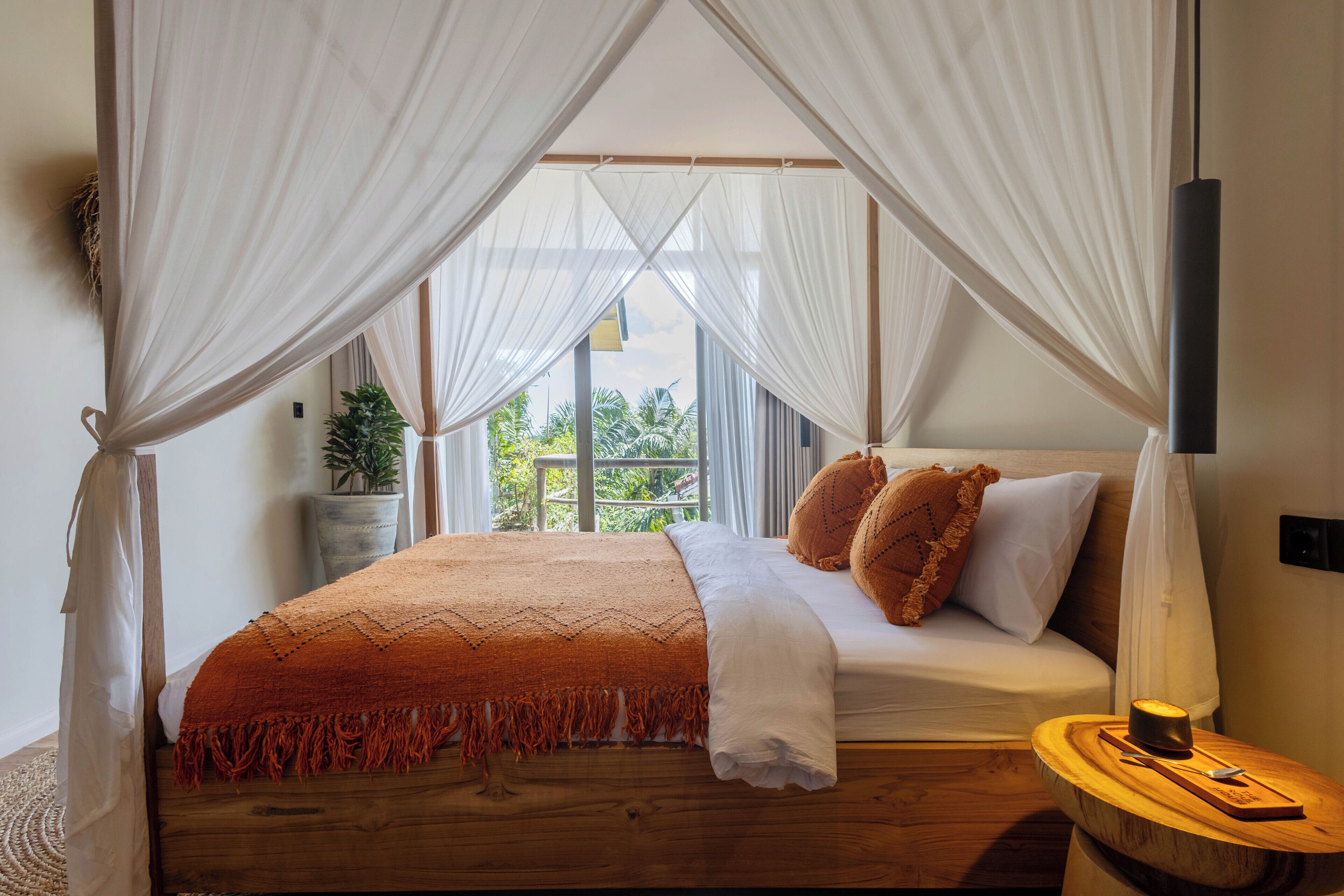Una cama con dosel, una mesita de noche con una vela y vistas al exterior con vegetación.