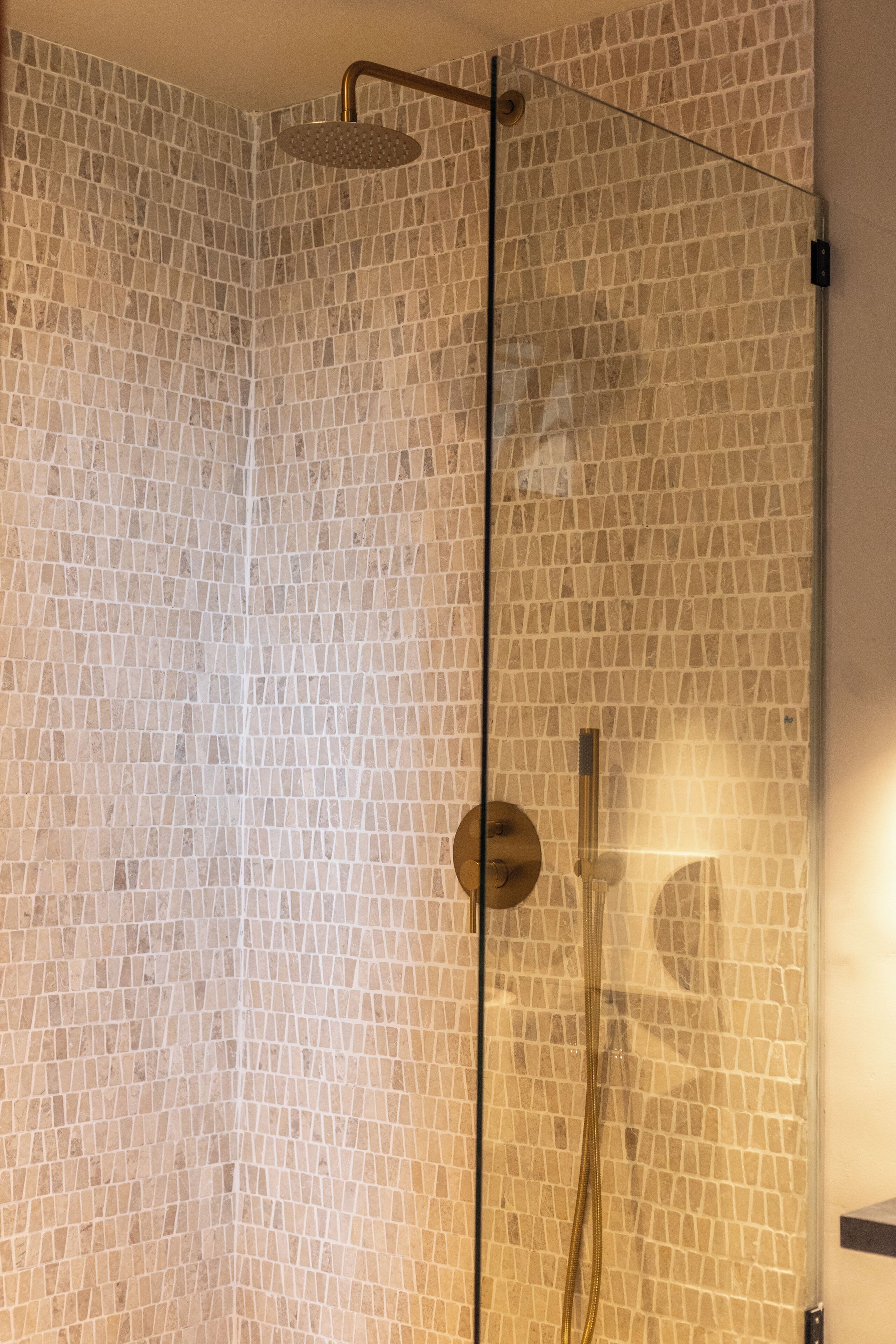 A shower with a glass door and a mosaic tile wall.