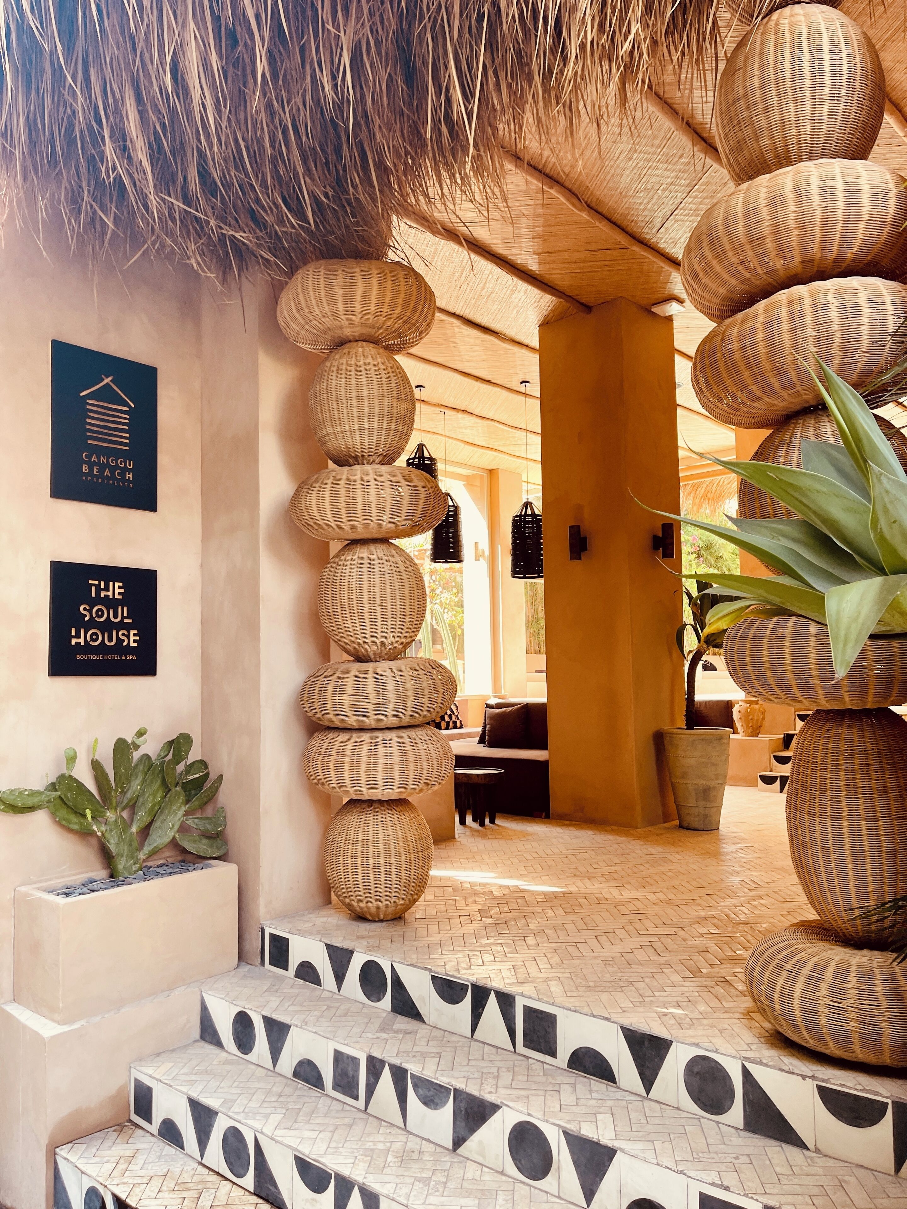A hotel entrance with a thatched roof, wicker decor, and a staircase with patterned tiles.