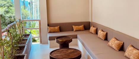 A modern outdoor seating area with a cushioned bench, a round wooden table, and a woven ceiling light fixture.