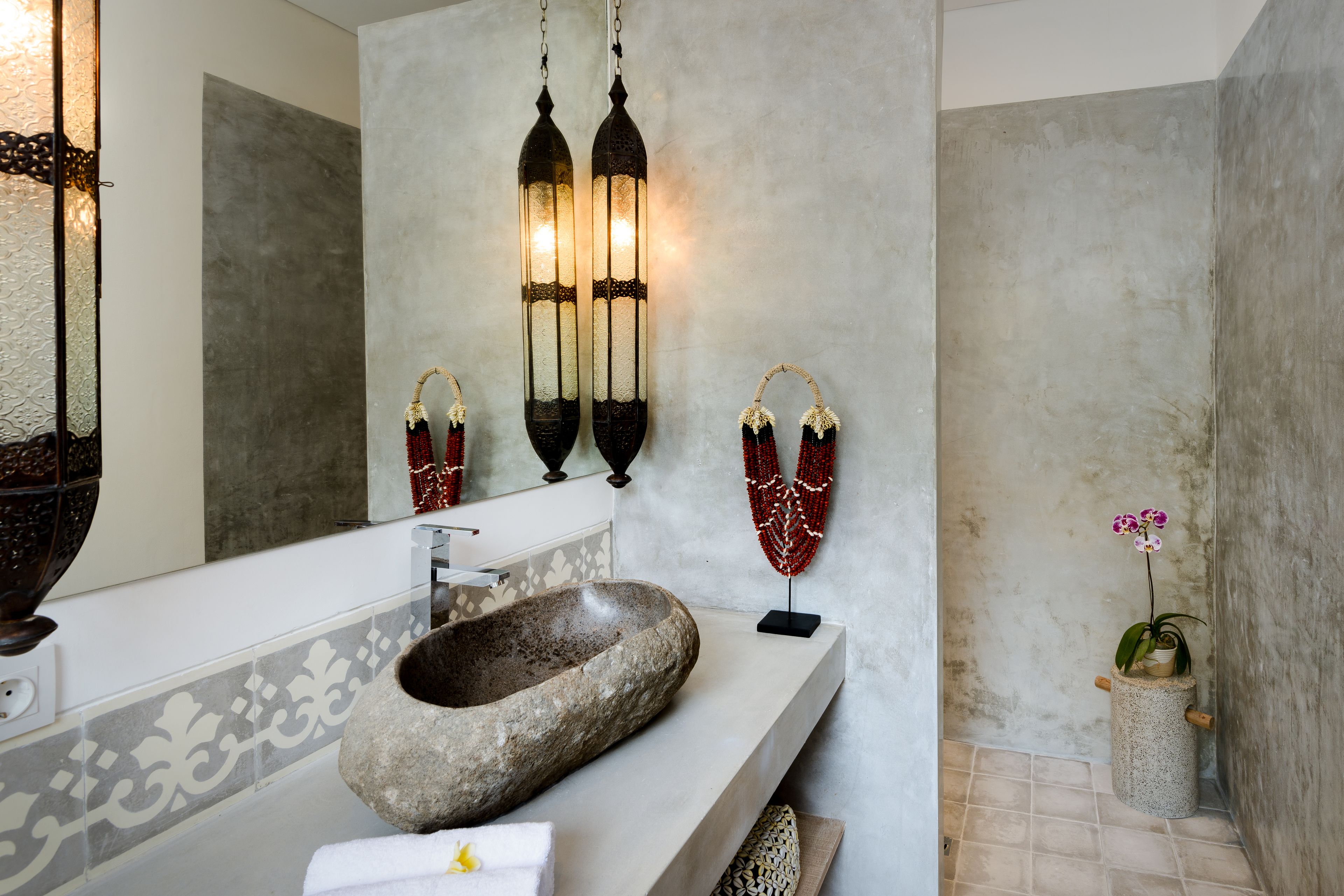 A bathroom with a stone sink, a mirror, and wall-mounted lights.