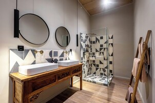 Un baño con tocador de madera, dos lavamanos, un espejo y una ducha con azulejos geométricos.