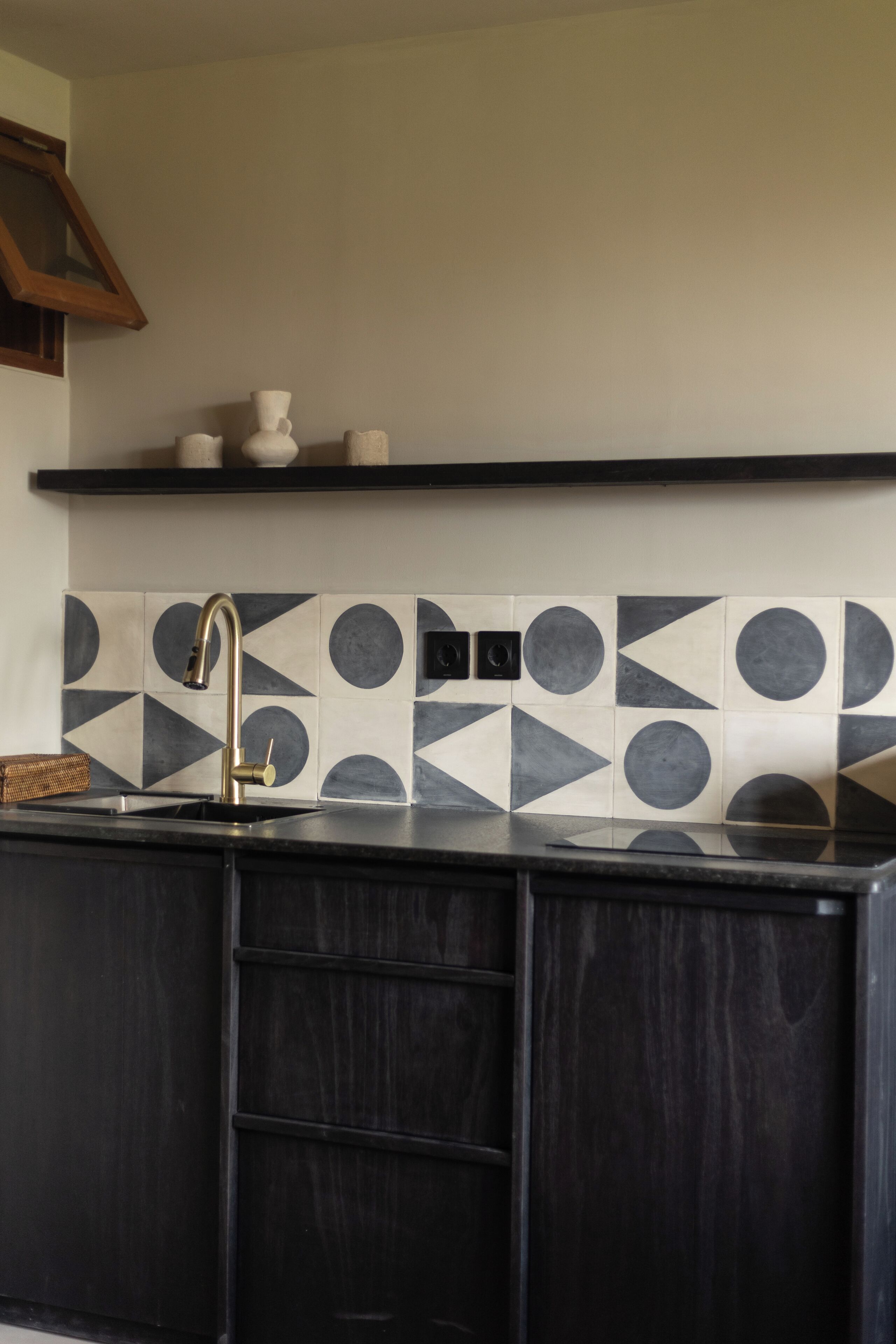 A kitchen with a black countertop, a gold faucet, and a geometric tile backsplash.
