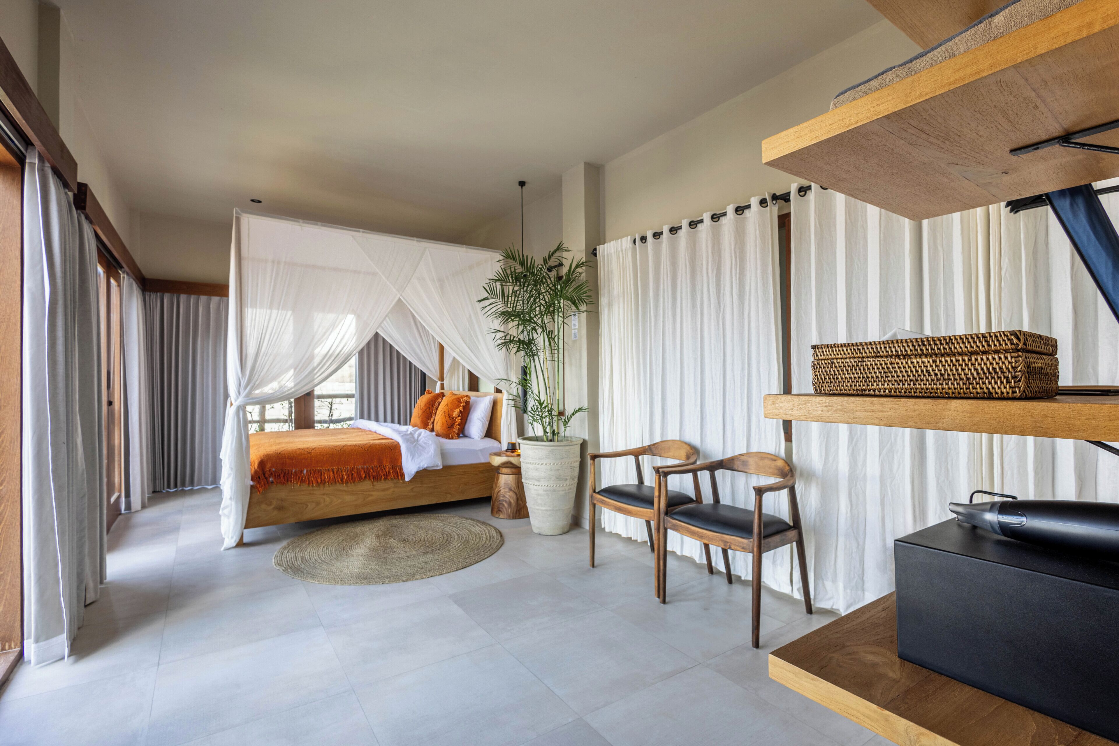 A bedroom with a bed, bedside table, chair, and a large potted plant.
