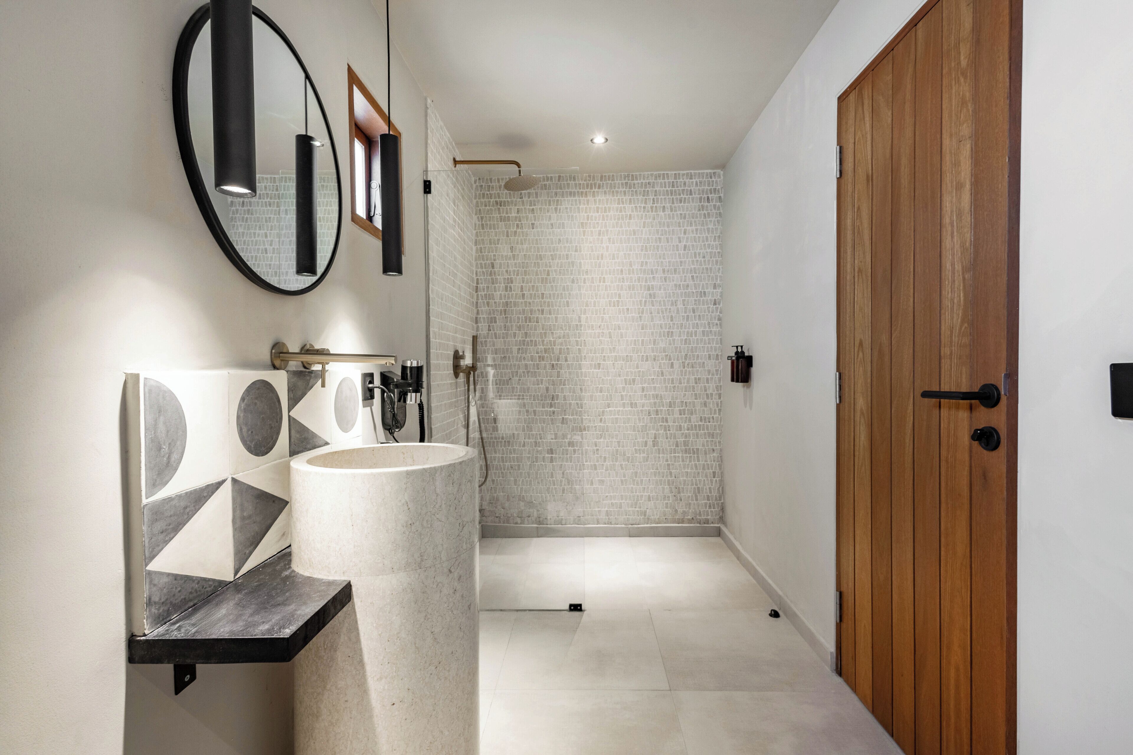 Un baño con lavamanos de mármol, un espejo y una zona de ducha con pared de ladrillo.