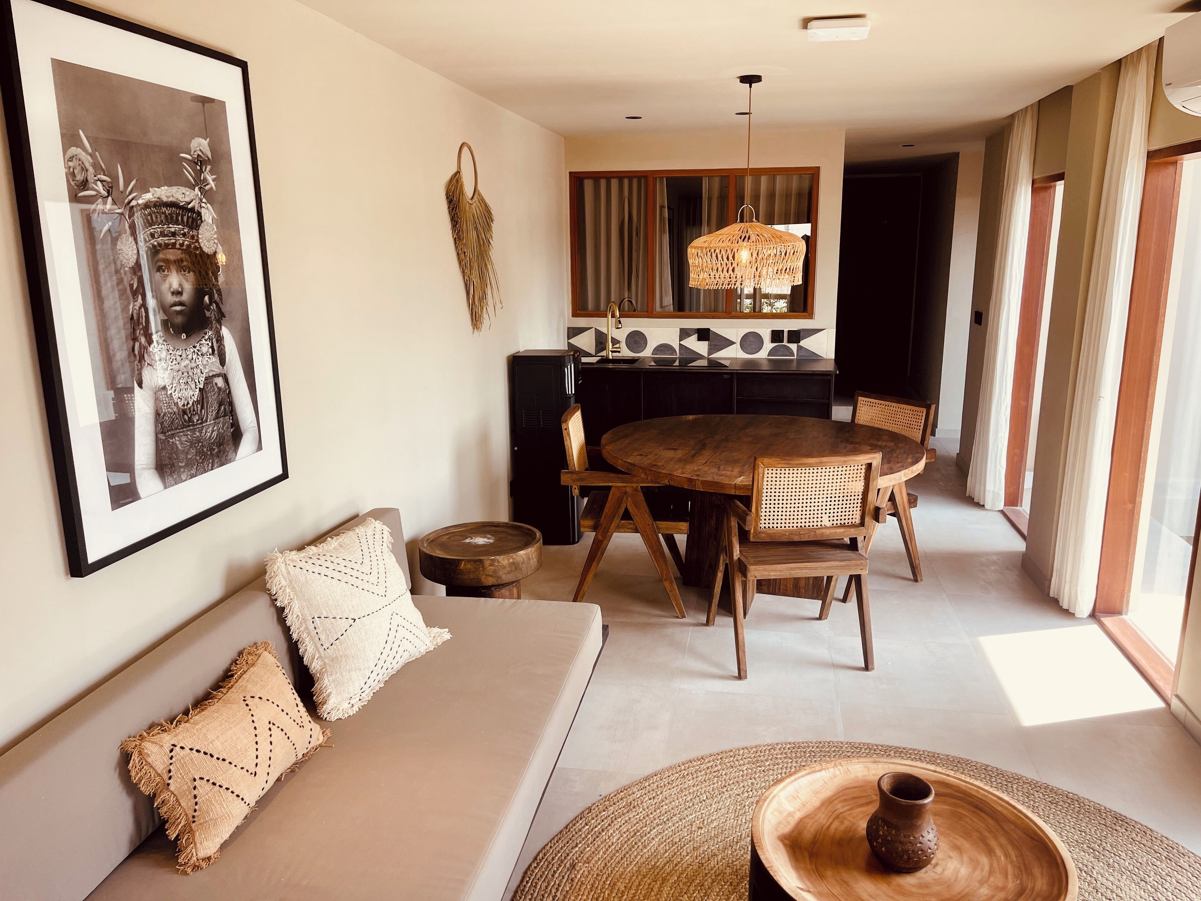 Ein modernes Wohnzimmer mit einer Couch, einem Esstisch und Stühlen. Im Hintergrund ist eine Küche mit Kühlschrank und einer Pendelleuchte zu sehen.