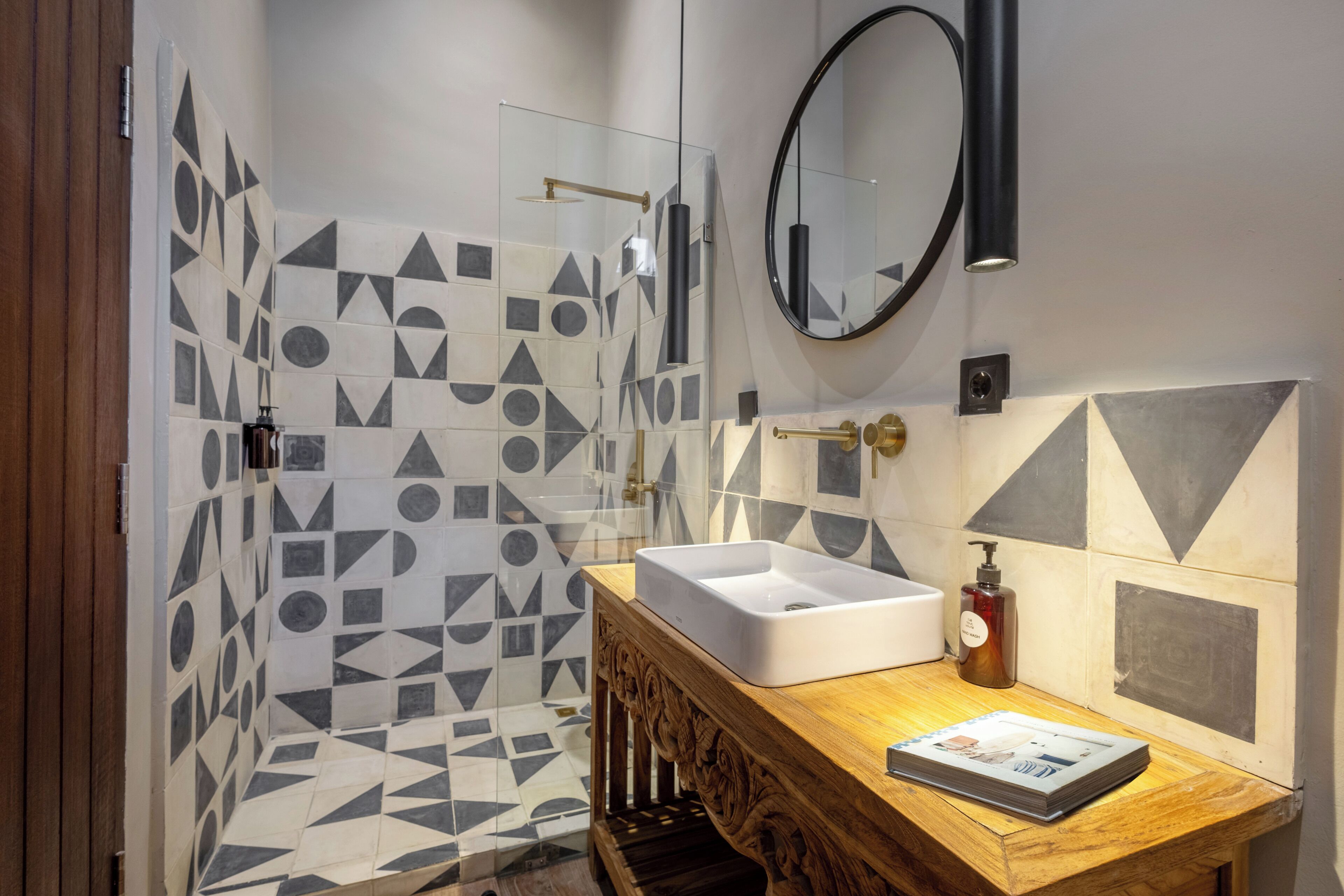 A modern bathroom with geometric patterned tiles, a wooden vanity with a sink, a mirror, and a shower with a glass door.
