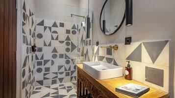 A modern bathroom with geometric patterned tiles, a wooden vanity with a sink, a mirror, and a shower with a glass door.