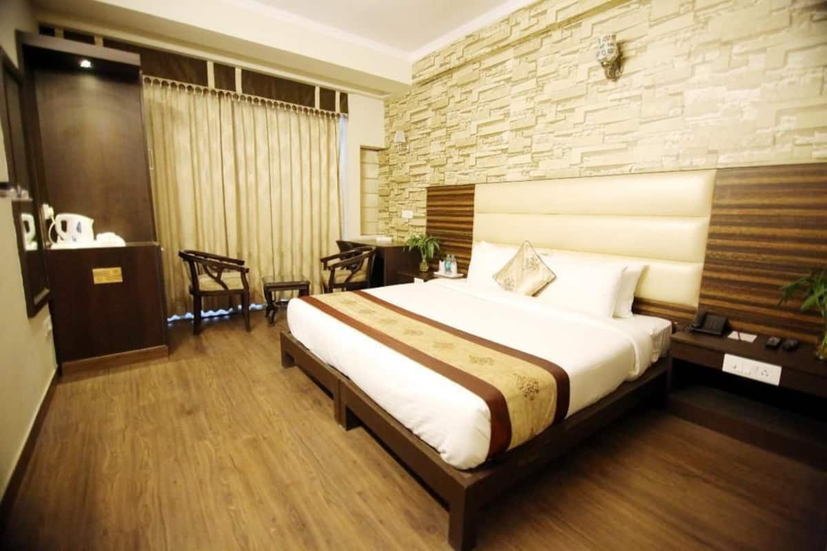 A hotel room with a large bed, a desk, and a chair. There is a stone wall behind the bed and a wooden floor.