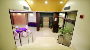 Un hall d’hôtel avec un escalier, un comptoir d’accueil et un espace détente comprenant une table violette.