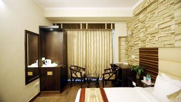 A hotel room with a bed, a desk with a chair, a small table, a mirror, and a stone wall.