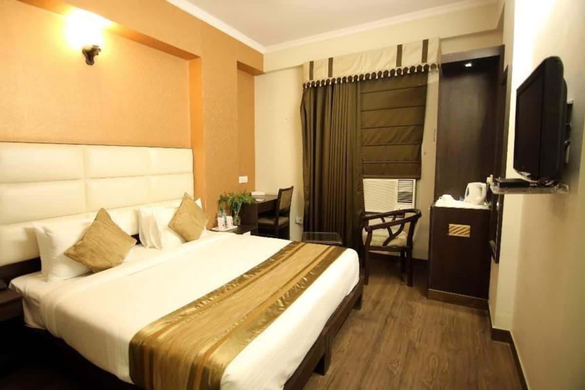 A hotel room with a large bed, a desk, a chair, a television, and a wardrobe.