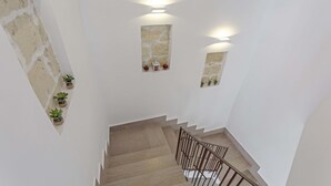Una escalera con escalones de madera y barandillas metálicas, flanqueada por paredes blancas y detalles de piedra.