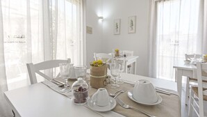 Un comedor con una mesa preparada para dos personas, con cristalería transparente, platos blancos y una cesta con flores.