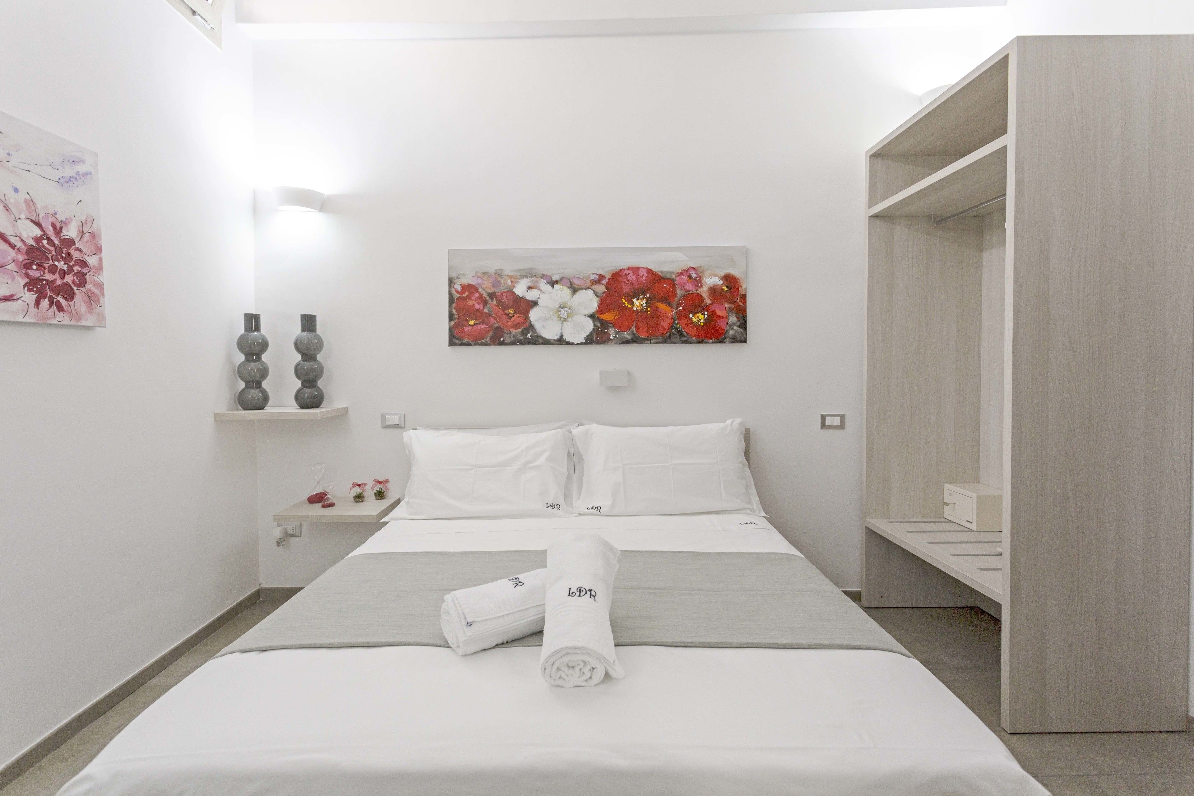 Una habitación de hotel moderna con una cama bien hecha, un cuadro de flores en la pared y un armario de madera.
