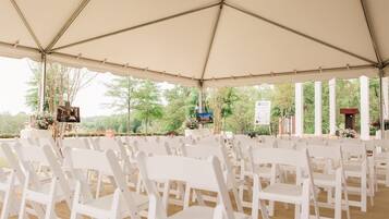 A tented outdoor event space with white chairs arranged in rows.