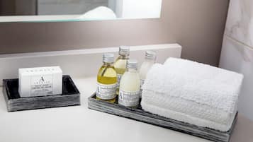 Un tocador de baño con una barra de jabón blanco, tres botellas de champú y una toalla blanca.
