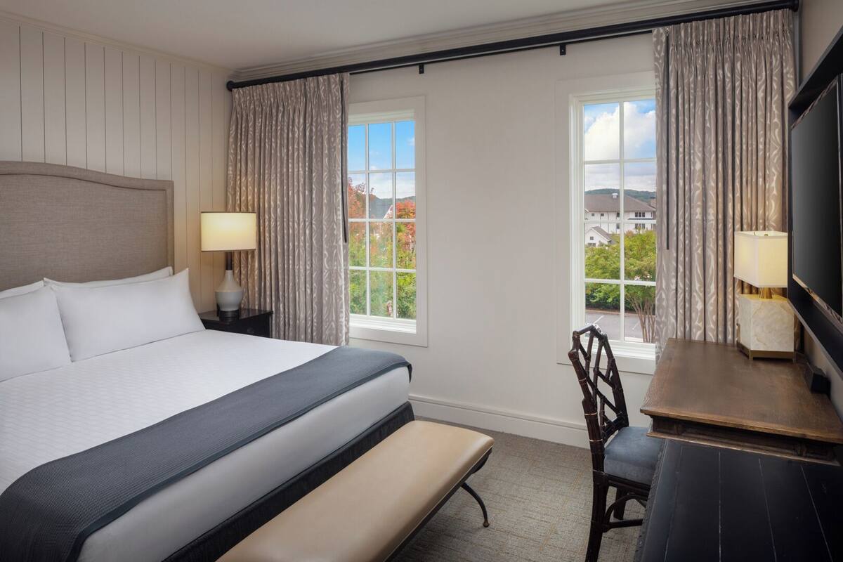 A hotel room with a large bed, two bedside lamps, a desk with a chair, and a TV.